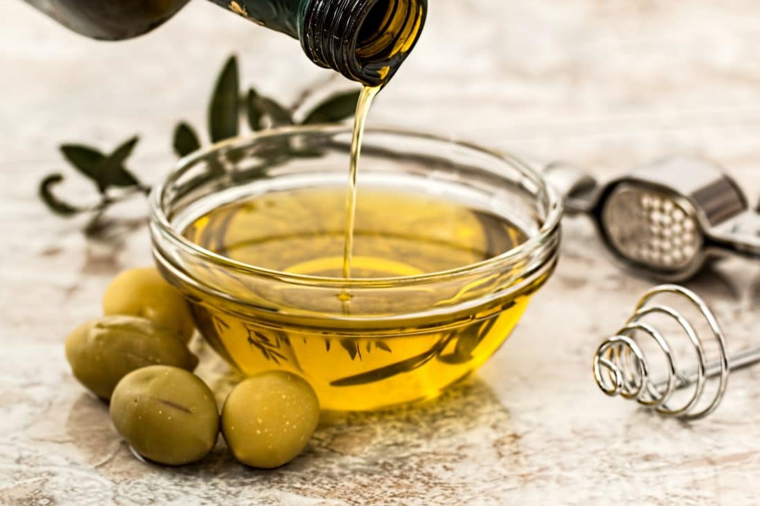 a bottle of olive oil being poured into a bowl of olives.